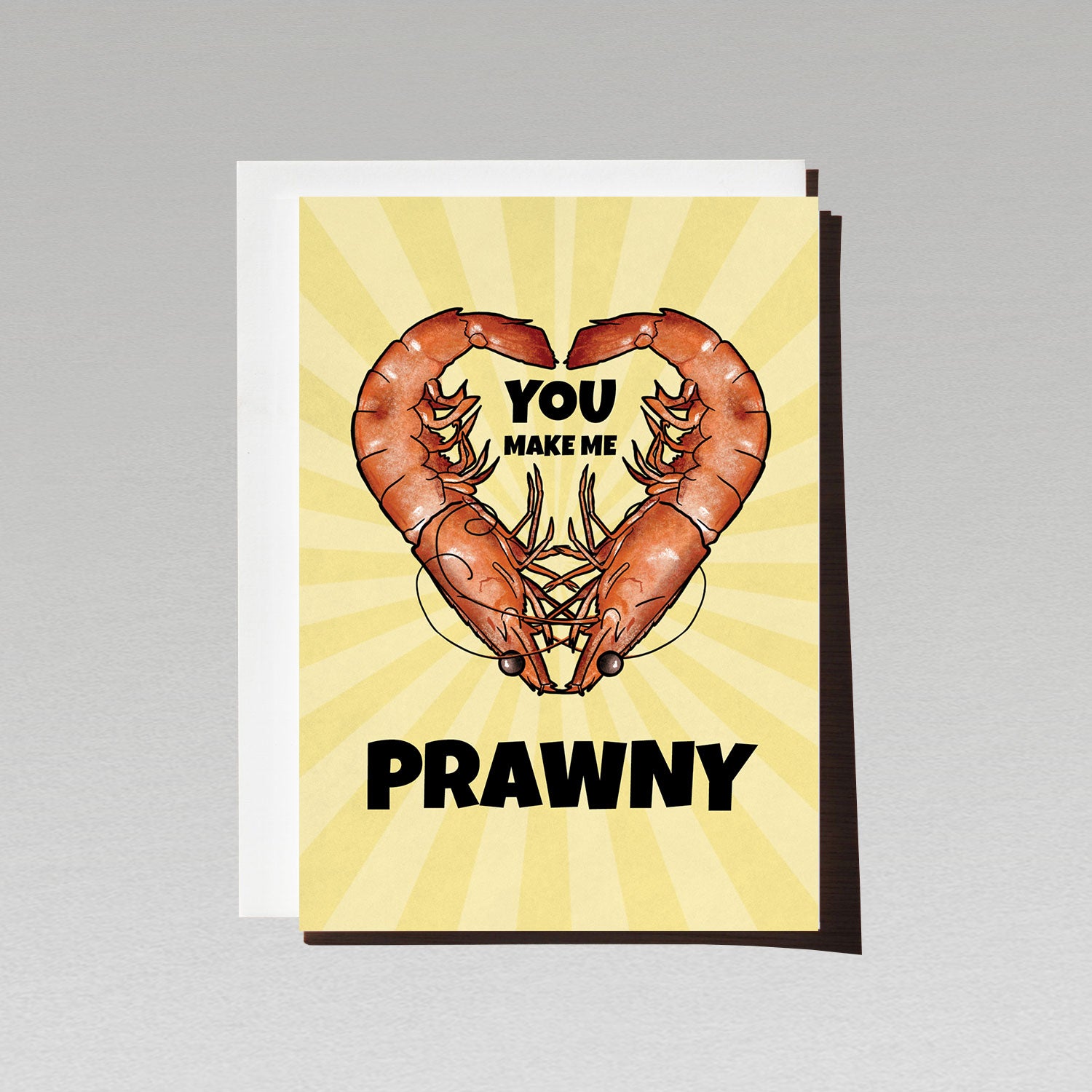 Two prawns facing each other to make a love heart shape on a pale yellow background with text You make me prawny